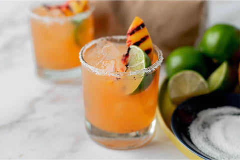 An orange margarita with a grilled peach slice